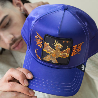 A person holds the Goorin Bros. Hell Hath No cap, a royal blue ombre hat with bold dragon embroidery, outstretched wings, and "FURY" on a black patch.