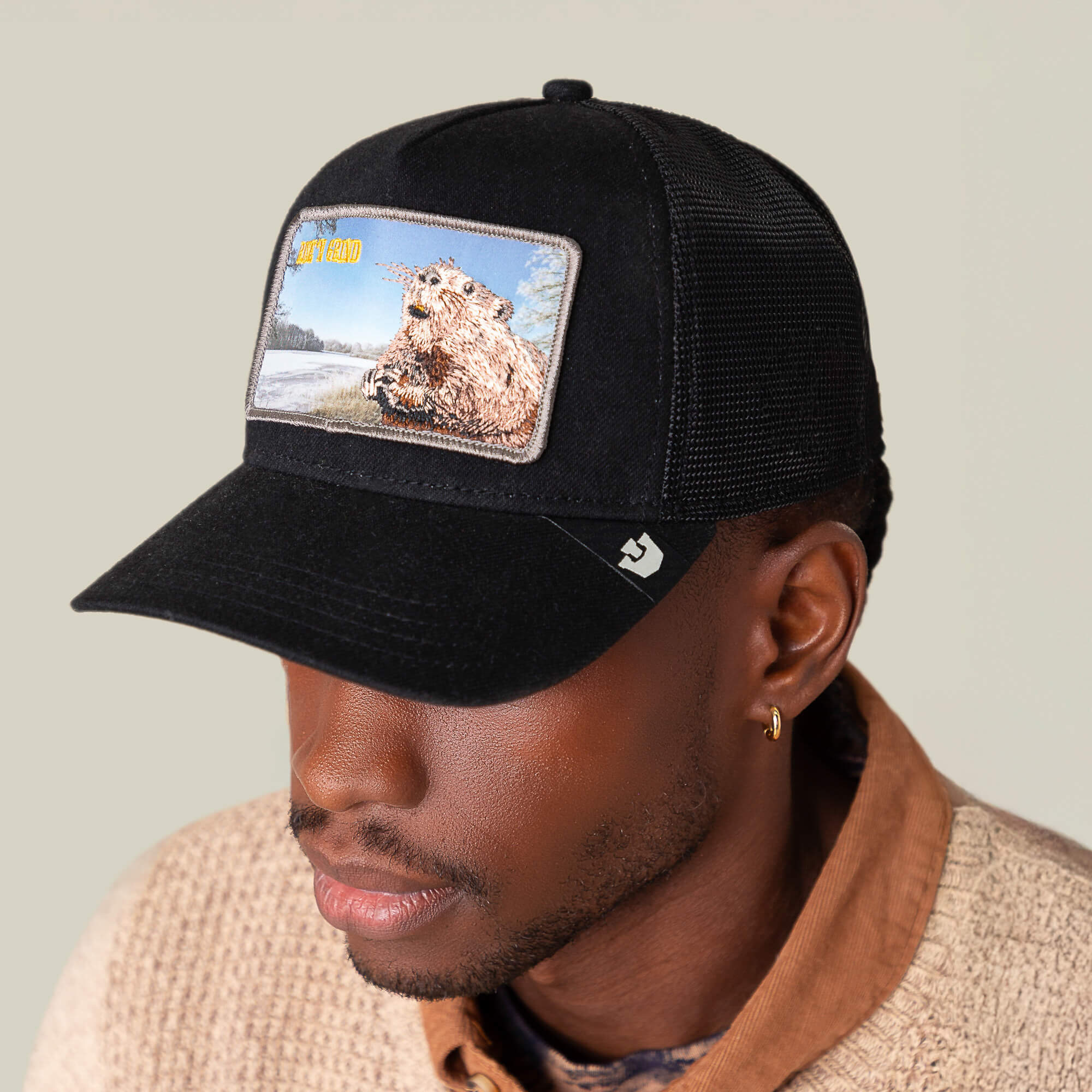 A person wears the Goorin Bros. Morning Wood black crown cap with a bear patch, styled with a beige textured sweater and brown collared shirt—perfect for that rise ’n grind energy.