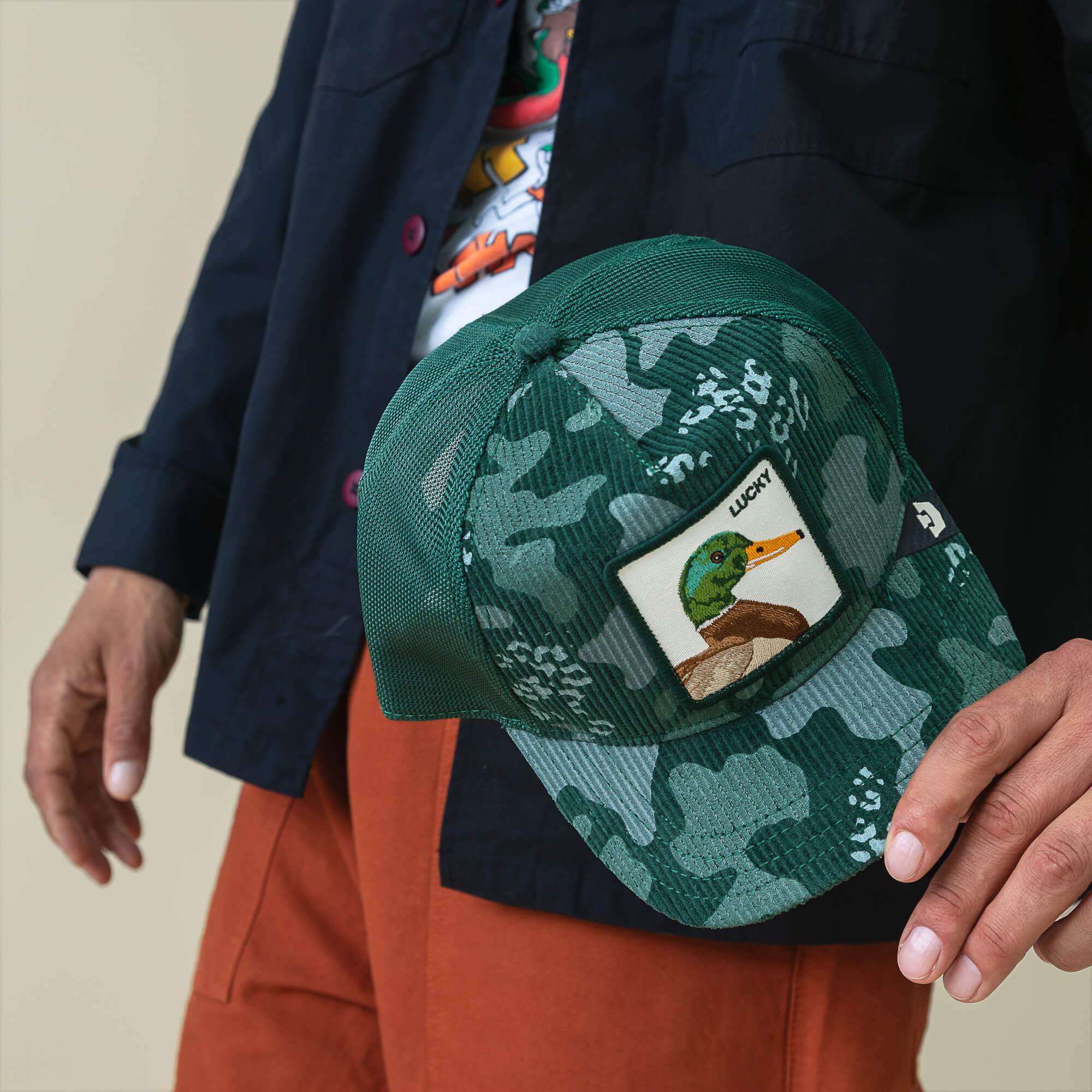 A person holding the Goorin Bros. Duck Camo corduroy hat with a forest green finish and camo patch.