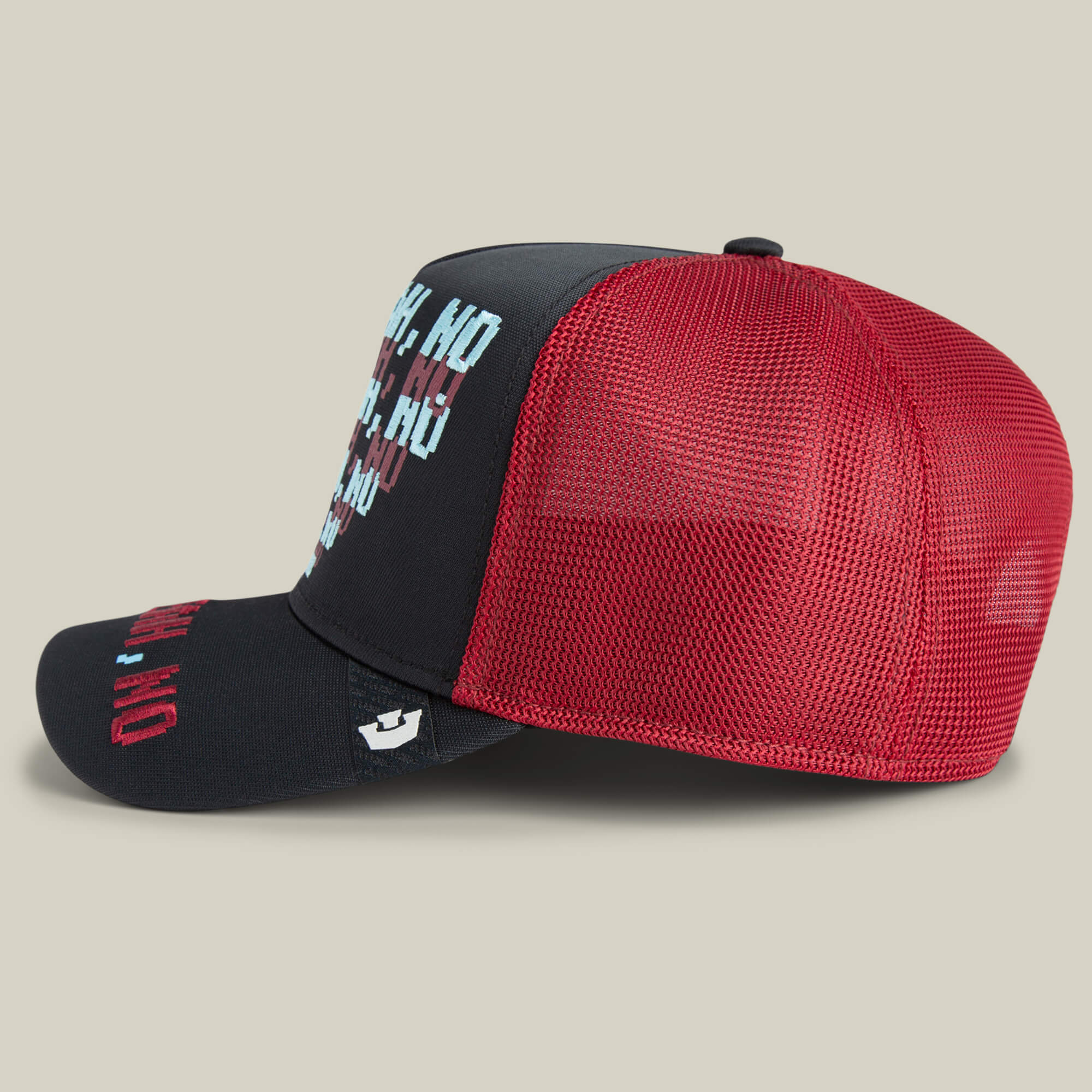 The Goorin Bros. Means No trucker hat features a black and red mesh design with white, blue, and red text on the front, shown from a side view against a plain background.