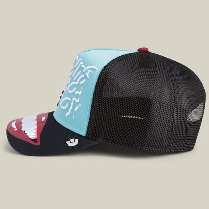 The Means Understood by Goorin is a mesh-back trucker hat with a blue front, black brim, white teeth graphic, and bold white side text—designed for those who wear confidence on top.