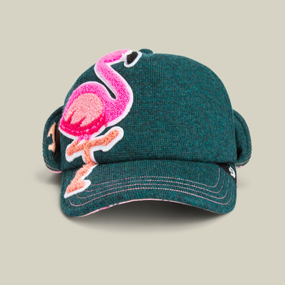 The Goorin Bros. "F is for Fake" trucker baseball cap in GUARD features a green fabric with ear flaps and a large pink flamingo patch on the front, shown against a plain beige background.