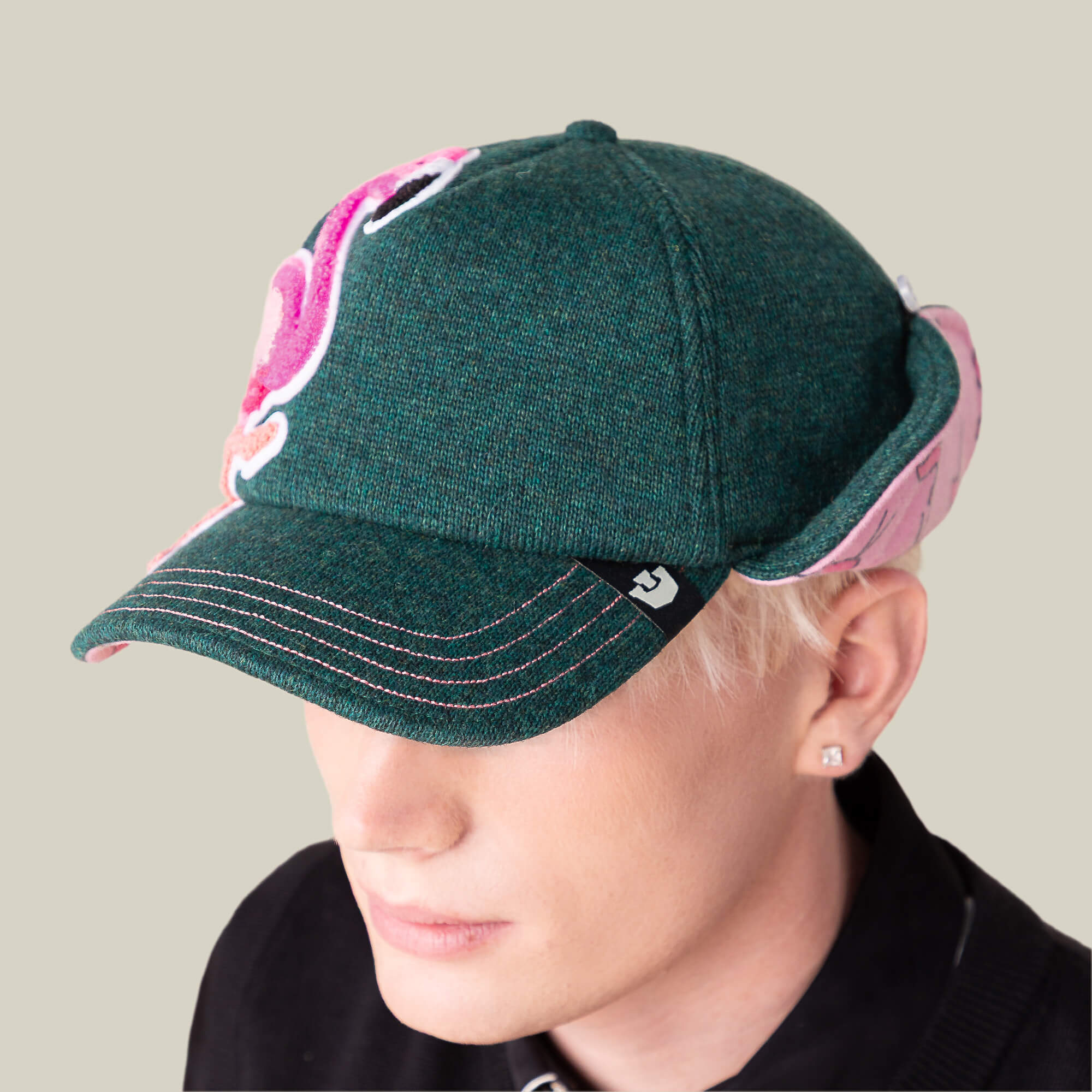 A person wearing the Goorin Bros. "F is for Fake" green and pink ear-flap trucker cap with white stitching and a black collared shirt, viewed from a slightly elevated angle.
