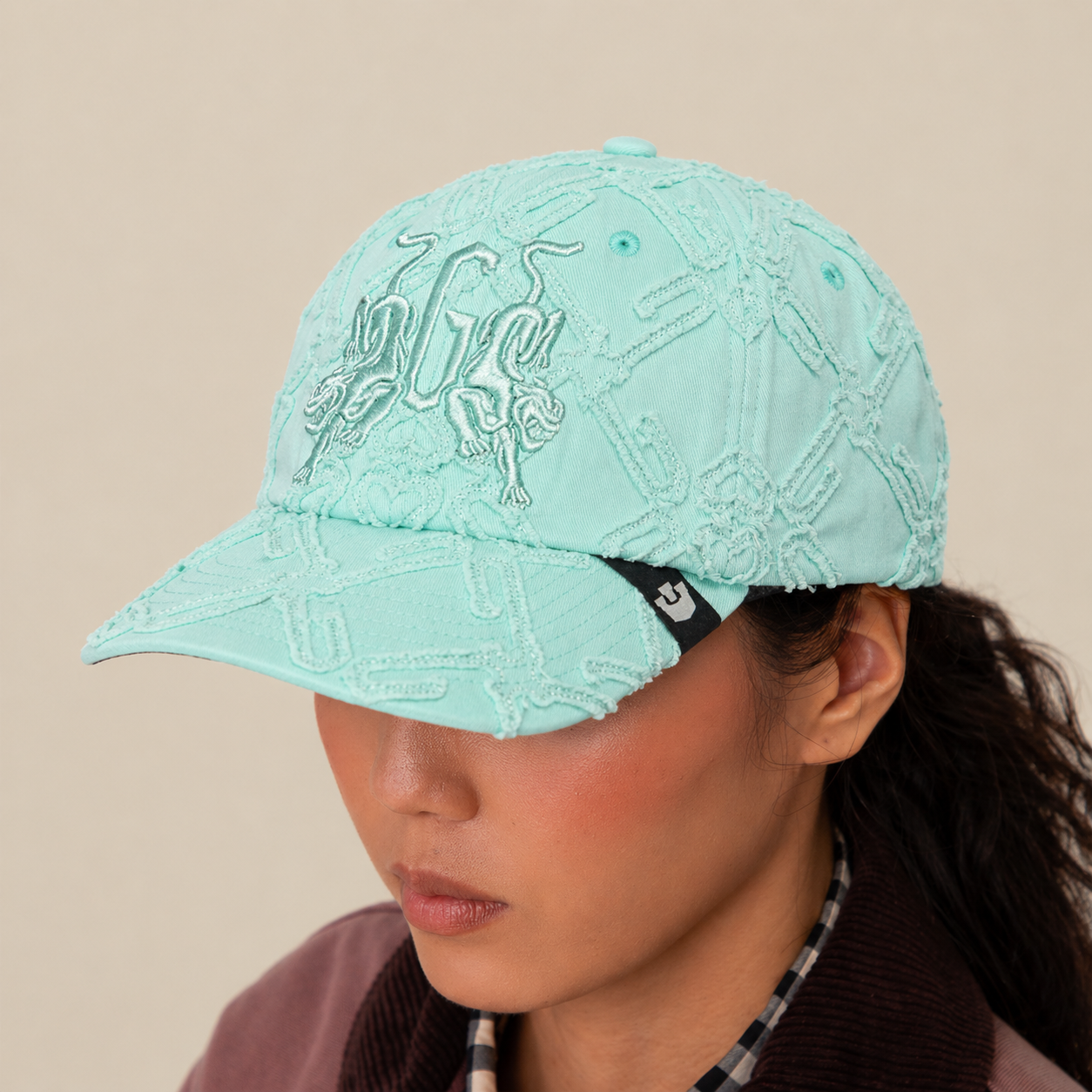 A person wears the Goorin Bros. "Future Baby Daddy" cap in light blue with all-over embroidery and a black tag, styled with a brown jacket and plaid shirt. The plain beige background highlights their main character energy.