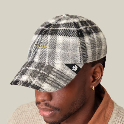 A person wearing the Goorin Bros. Bespoke Wordmark cap—a black and white plaid wool blend hat featuring a small logo patch on the side and gold embroidered text on the front.