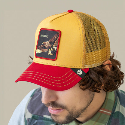 A man wearing Goorin Bros.' The Faithful Eagle hat, featuring a yellow and red design with an eagle patch labeled "FAITHFUL," and a plaid shirt, faces slightly downward against a plain background.