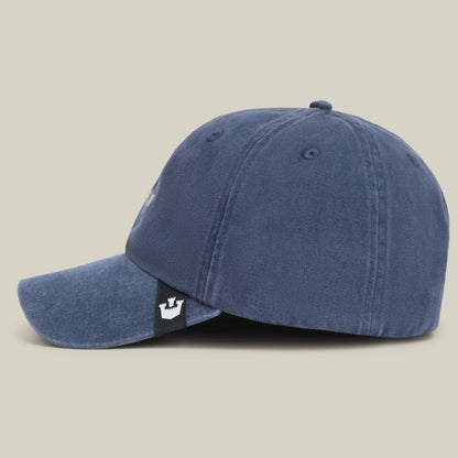 A blue Papa Cap Italiano by Goorin Bros. shown from the side, featuring a black tag with a white crown logo near the adjustable strap at the back—ideal for fans of distinctive style.