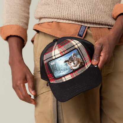 A person in a flannel jacket holds the Goorin Bros. Cabin Fever plaid trucker hat, which displays an image of a tiger and "NIGHT OWL" on the front patch, capturing rugged comfort and bold style.