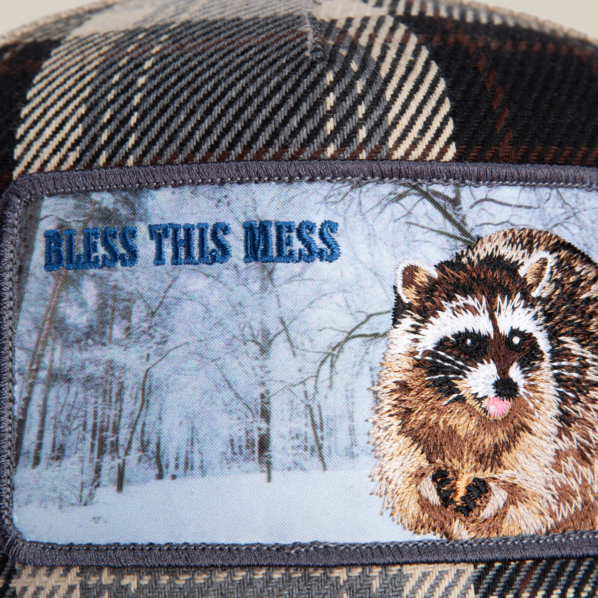 The Free Spirited patch by Goorin Bros. features a raccoon, the phrase "Bless This Mess," and a plaid crown, all set against a snowy forest scene for a cozy, rustic vibe.
