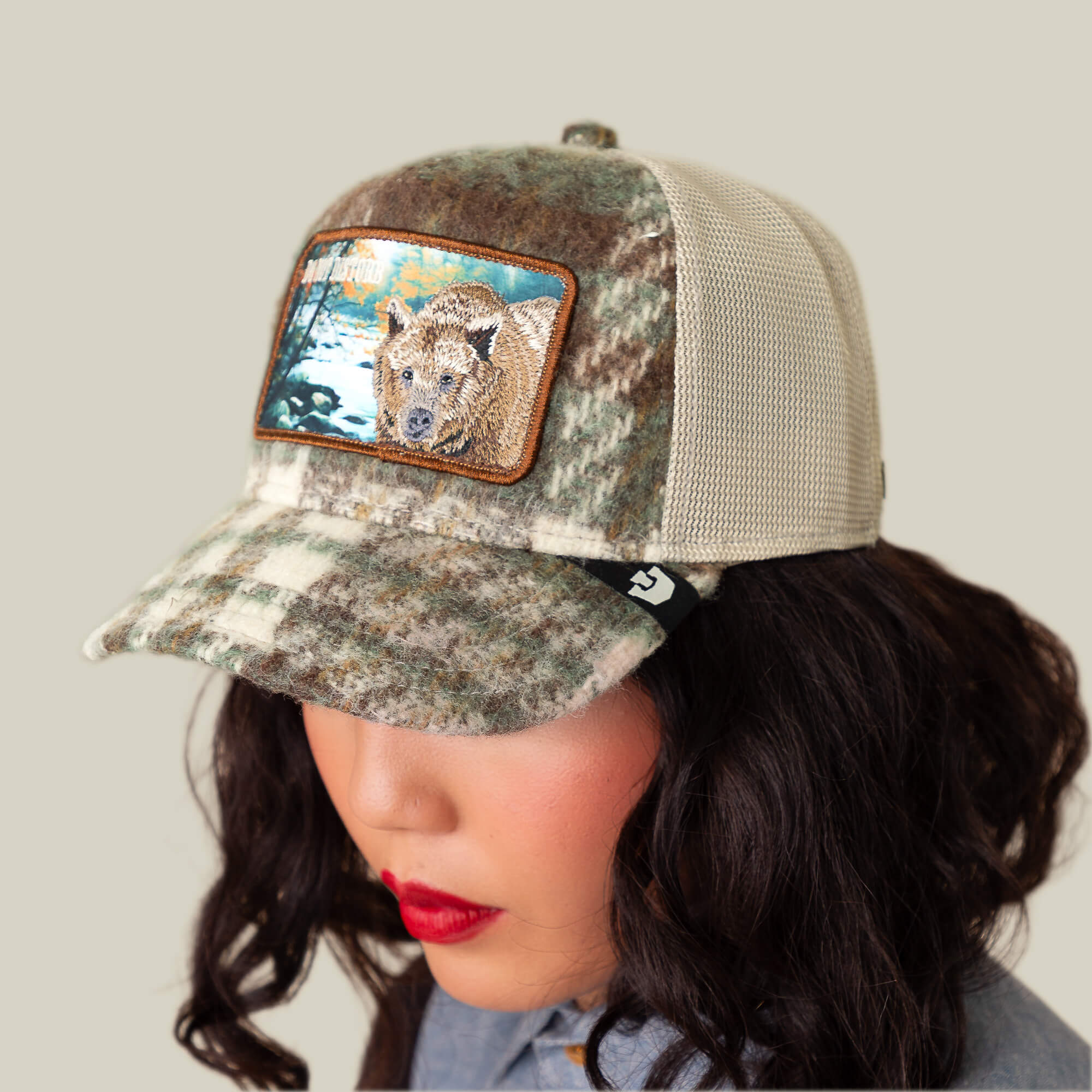 Someone wears the Goorin Bros. "Don't Poke the Bear" camo plaid cap with a bear-in-nature patch, exuding flannel-inspired comfort against a plain backdrop.