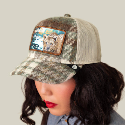 Someone wears the Goorin Bros. "Don't Poke the Bear" camo plaid cap with a bear-in-nature patch, exuding flannel-inspired comfort against a plain backdrop.