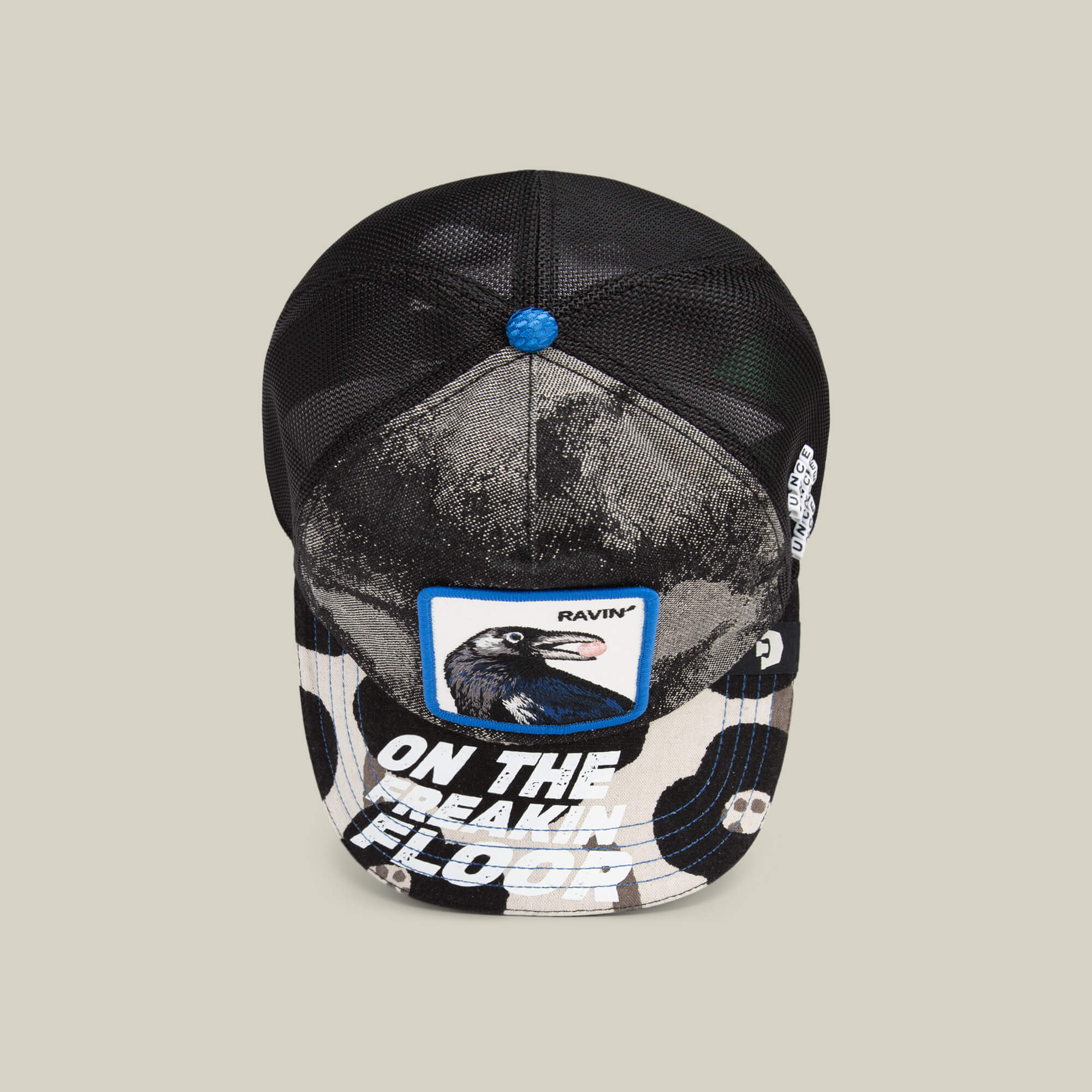 The “Techno” hat by Goorin Bros. is a black mesh trucker with a raven patch, blue button, and “ON THE FREAKIN FLOOR” on the brim—ideal for raves or standout festival style.