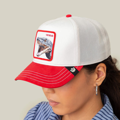 Sporting the Goorin Bros. Suede Snake trucker cap in white and red with a snake patch labeled "VICIOUS," this person radiates predator energy. Smooth suede adds comfort, while hoop earrings complete the look.