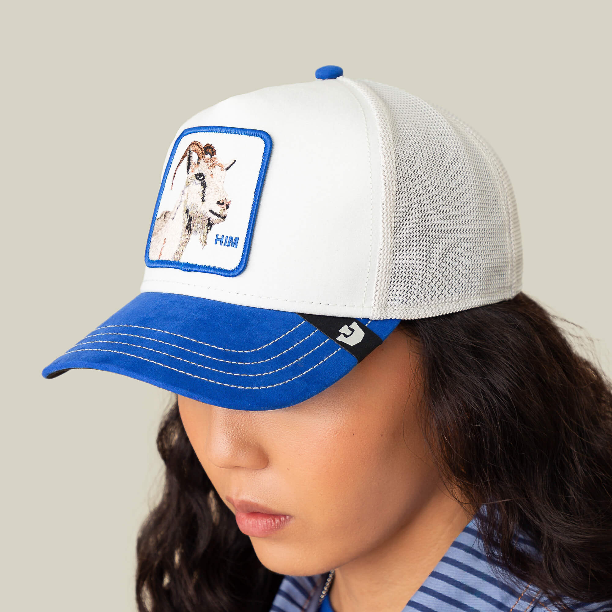A person wears the Goorin Bros. Suede Goat hat, featuring a white crown, blue suede brim, a goat patch, and "HIM" on the front.