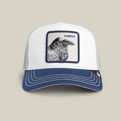 The Goorin Bros. Tricolor Raven hat is a white mesh trucker cap with a navy bill, featuring a raven patch and "CUERVO" above it, shown on a plain beige background.