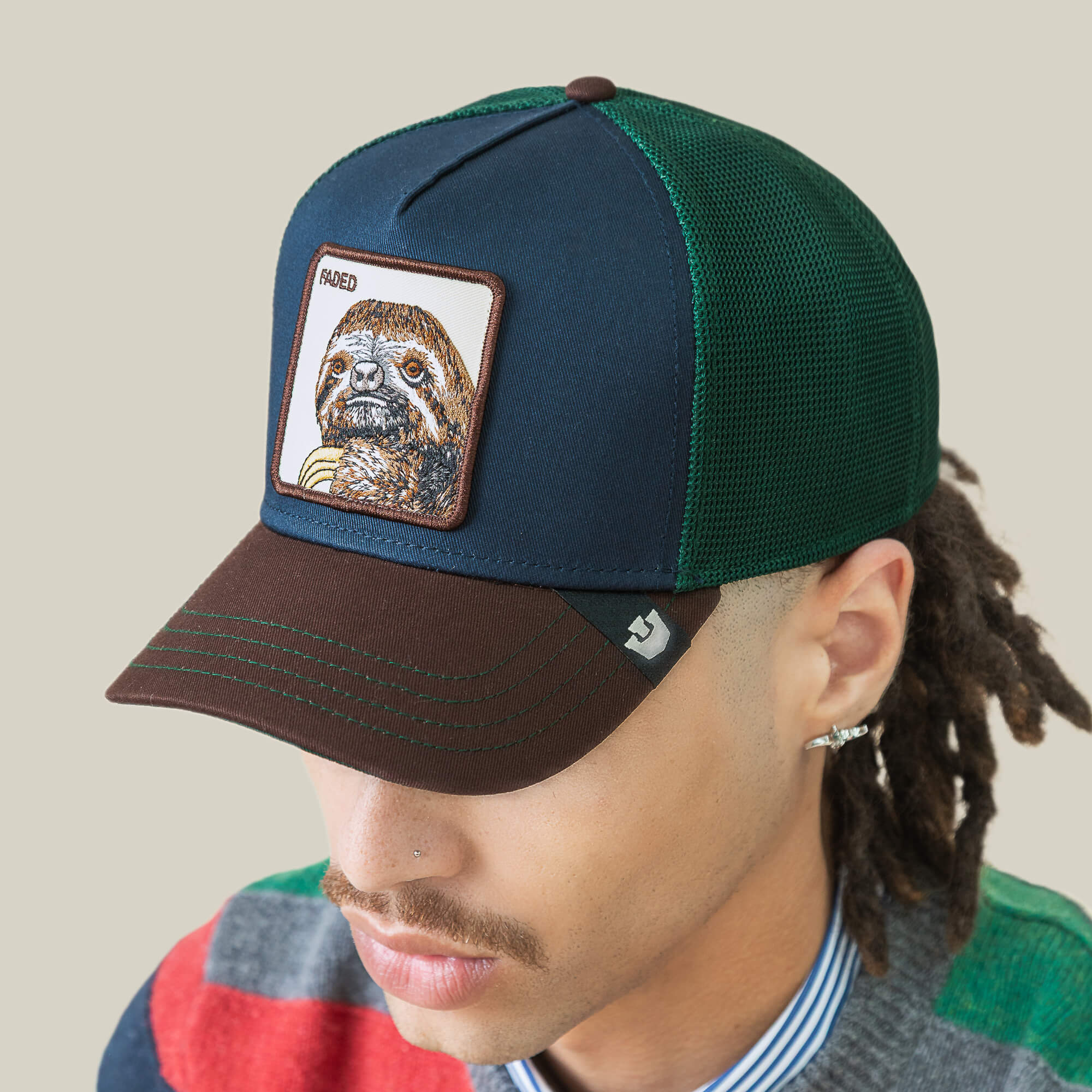 Someone wears the Goorin Bros. Tricolor Sloth hat, featuring green and brown colors with a sloth patch on the front, while looking downward.