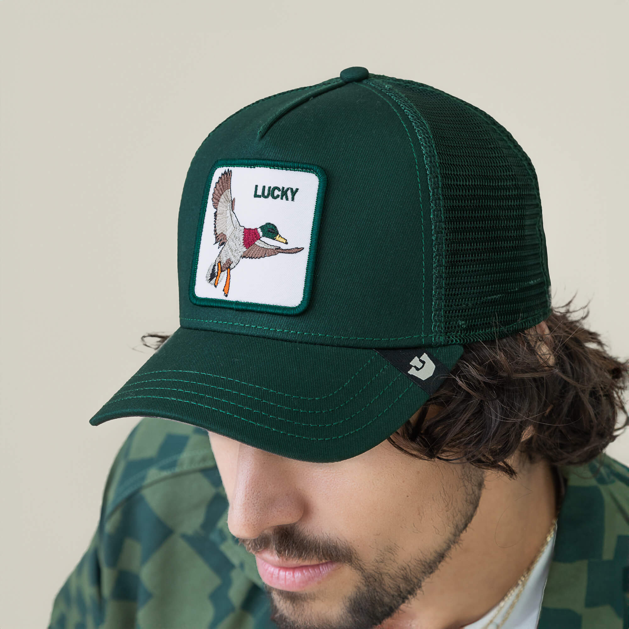 A man wears The Lucky Duck mesh trucker hat by Goorin Bros., featuring a flying duck patch and the word LUCKY on the front—a stylish charm for every adventure.