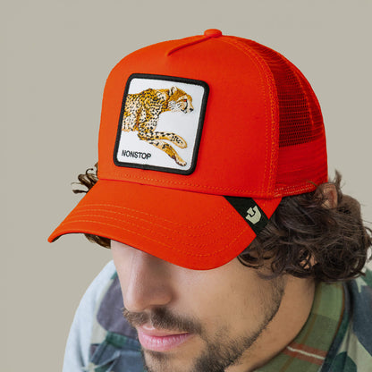 A man in a plaid shirt wears Goorin Bros. The Nonstop Cheetah, an orange fabric trucker cap featuring a cheetah patch labeled NONSTOP on the front.