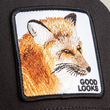 Close-up of the Goorin Bros. "Good Looks Fox" trucker hat, featuring an embroidered fox head patch with "GOOD LOOKS" in black text at the lower right corner.