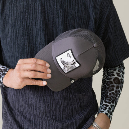 A person in a dark textured shirt with leopard print sleeves holds a stylish Goorin Bros. cap, the “Silver Foxxx,” featuring a wolf patch and the words SILVER WOLF, echoing the refined allure of the Silver Fox.