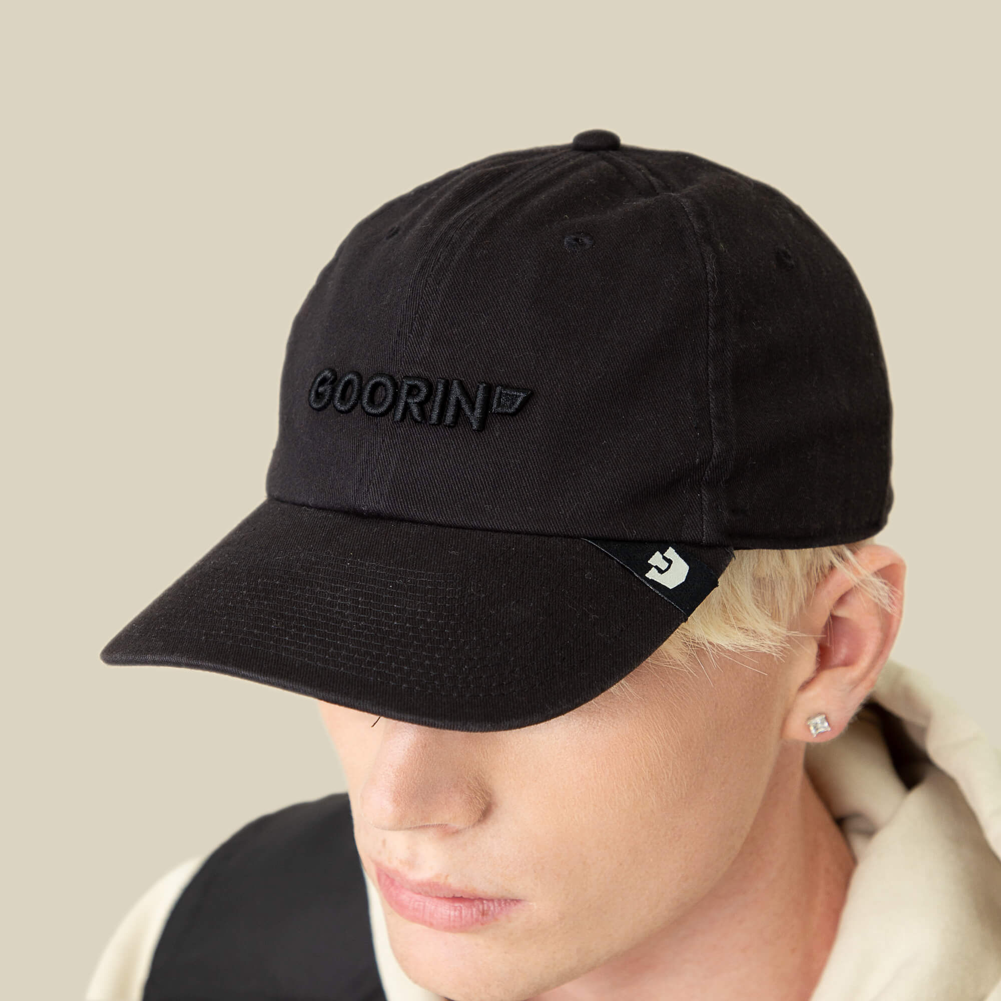 A person wearing the Goorin Bros. Papa Core black hat with a soft crown and curved brim, paired with a light hoodie, looks downward against a plain beige background.