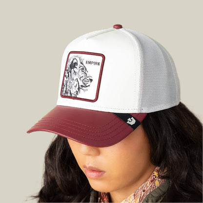 A person wears the Goorin Bros. Courtside Empire trucker hat, featuring a leather-look crown and an EMPIRE lion patch, ideal for sneaker culture fans, set against a plain beige background.