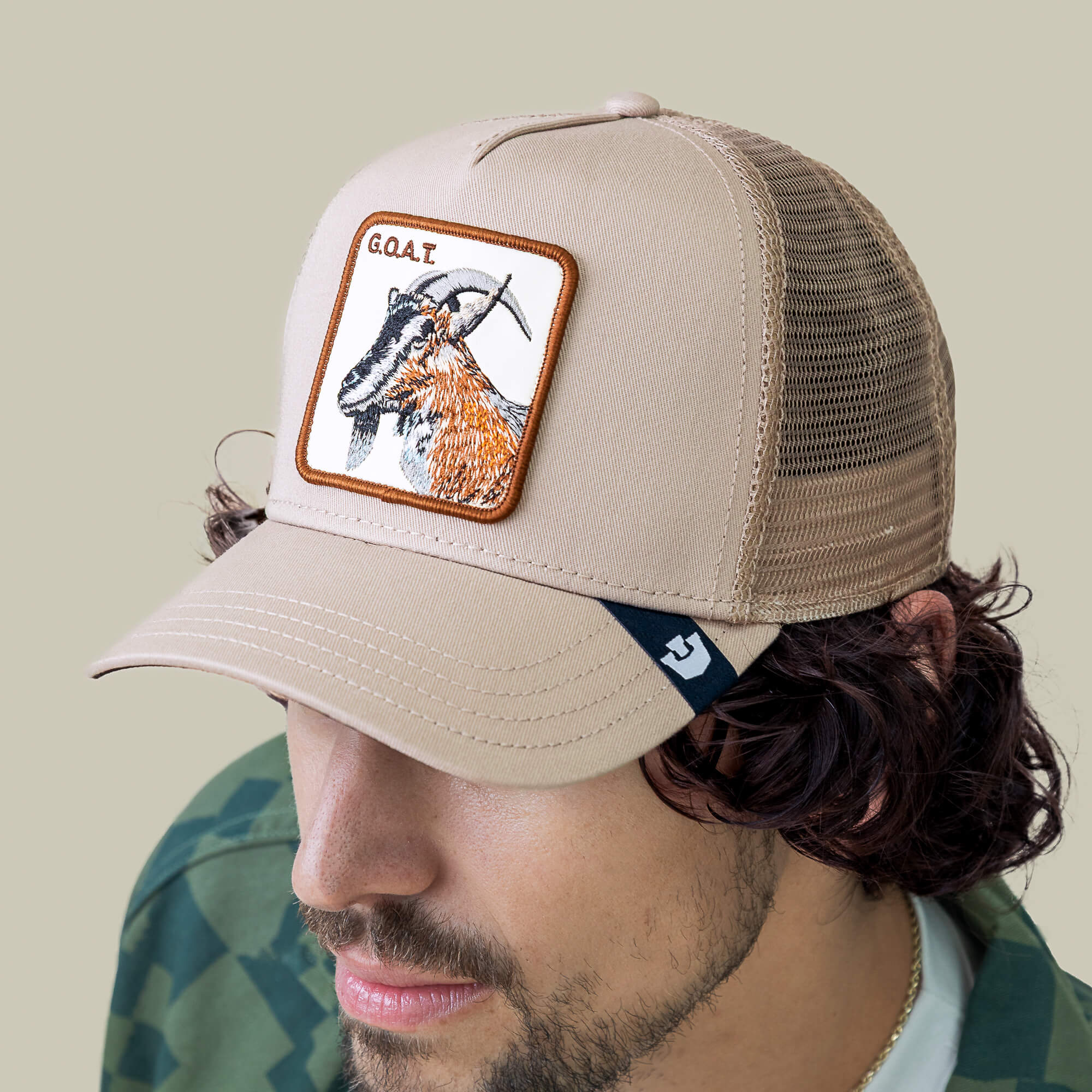 A man wears The G.O.A.T trucker hat by Goorin Bros., featuring a bold embroidered goat patch and "GOAT" text, viewed from above against a plain neutral background.