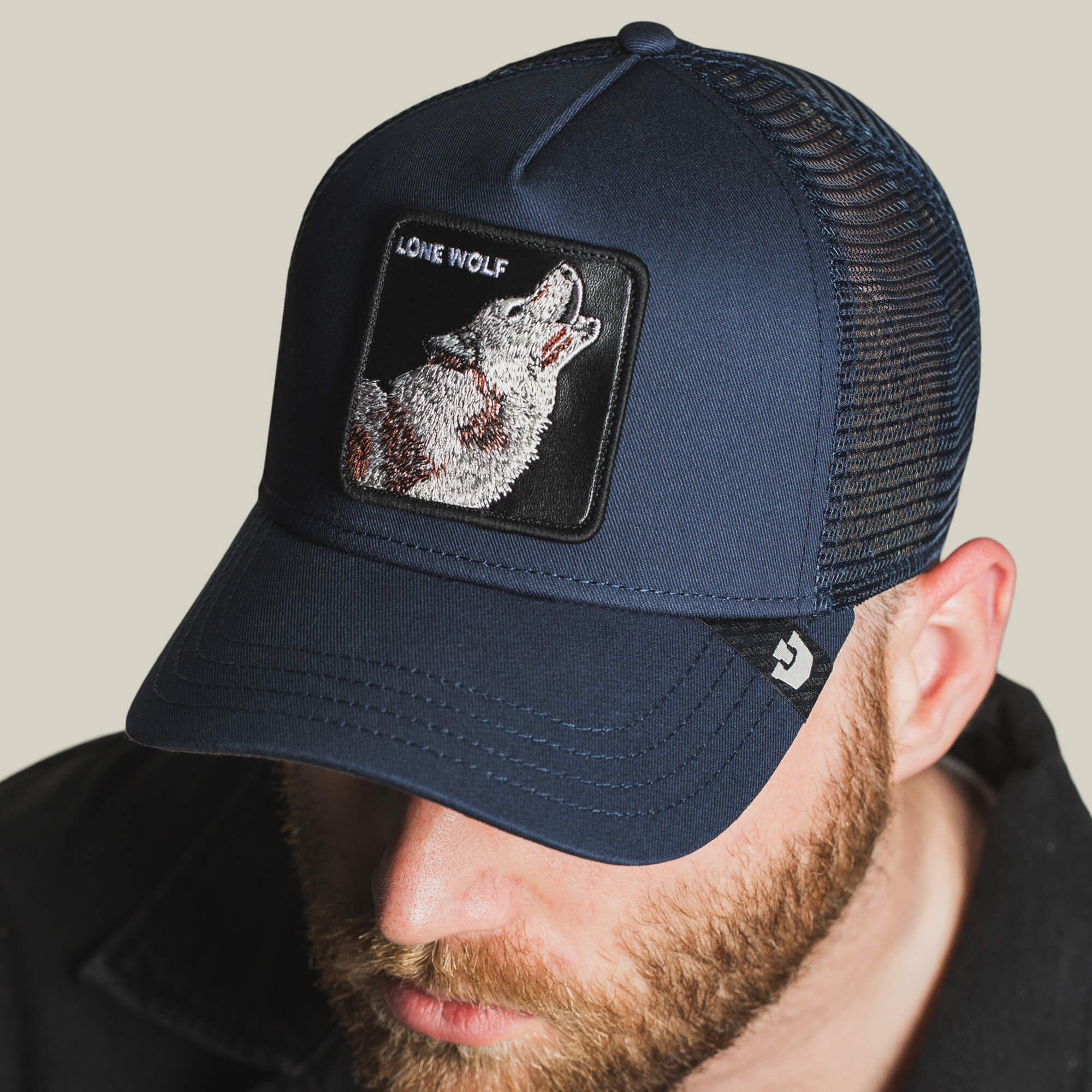 Man wears The Lone Wolf trucker cap by Goorin Bros., a navy mesh hat with a howling wolf patch and "LONE WOLF" on the front—ideal for adding outlaw energy to your style.