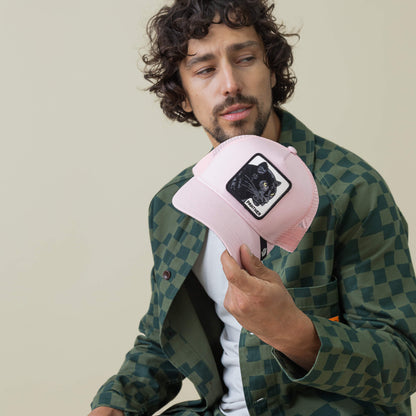 A man with curly hair in a green checkered jacket holds and examines the Goorin Bros. Panther Trucker cap, featuring a black cat patch.
