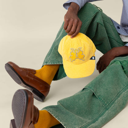A person sitting on the floor holding a Goorin Bros. Bleacher Report hat with a corduroy crown.