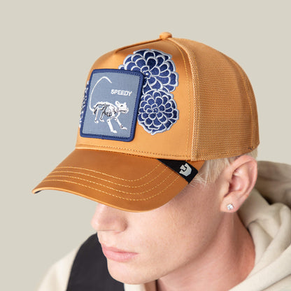 A person wearing the Goorin Bros. Dia De Speedy tan mesh baseball cap, featuring blue floral embroidery on the crown and a patch with a cat skeleton and "SPEEDY.