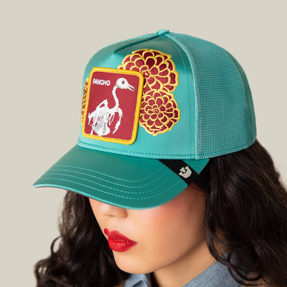 Wearing the Goorin Bros. "Dia De Pancho" teal mesh cap with floral embroidery and a skeleton bird patch, this person channels a rebel spirit, their face partly hidden beneath the hat.