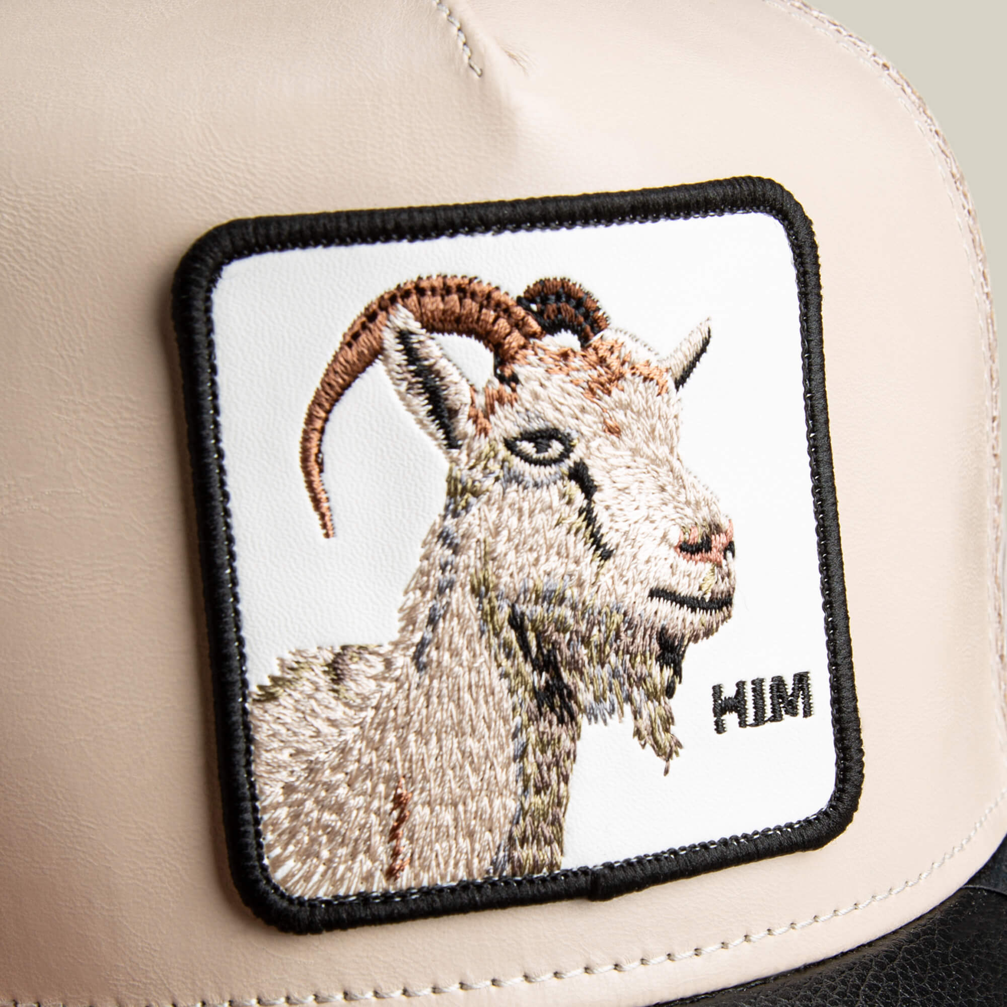 The Courtside Him cap by Goorin is beige with a square GOAT patch showing an embroidered goat and "HIM" in black, finished in a stylish tunnel fit.