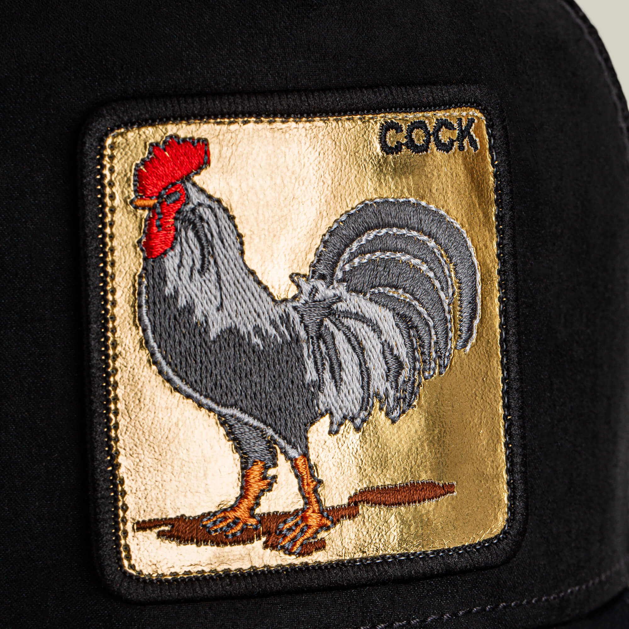 The Goorin Bros. "Golden Cock" patch features an embroidered rooster and golden lettering on a black fabric surface.