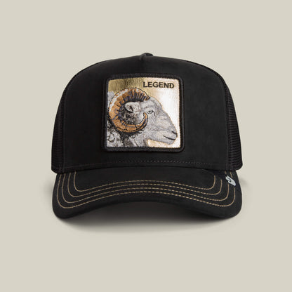 The Goorin Bros. Golden Legend black trucker hat features gold-stitched tan accents, a front patch with a ram's head, and "Golden Legend" embroidered above it on the front panel.
