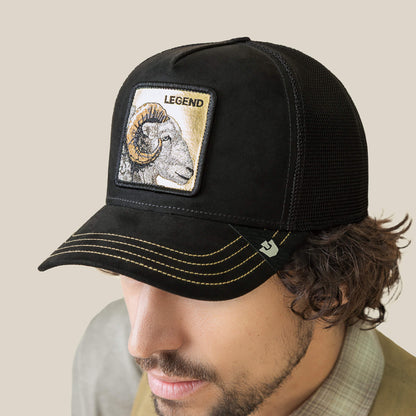 A man wears the Goorin Bros. Golden Legend—a black trucker hat with a gold stitched ram patch and “Golden Legend” embroidered above it, honoring fearless leaders everywhere.