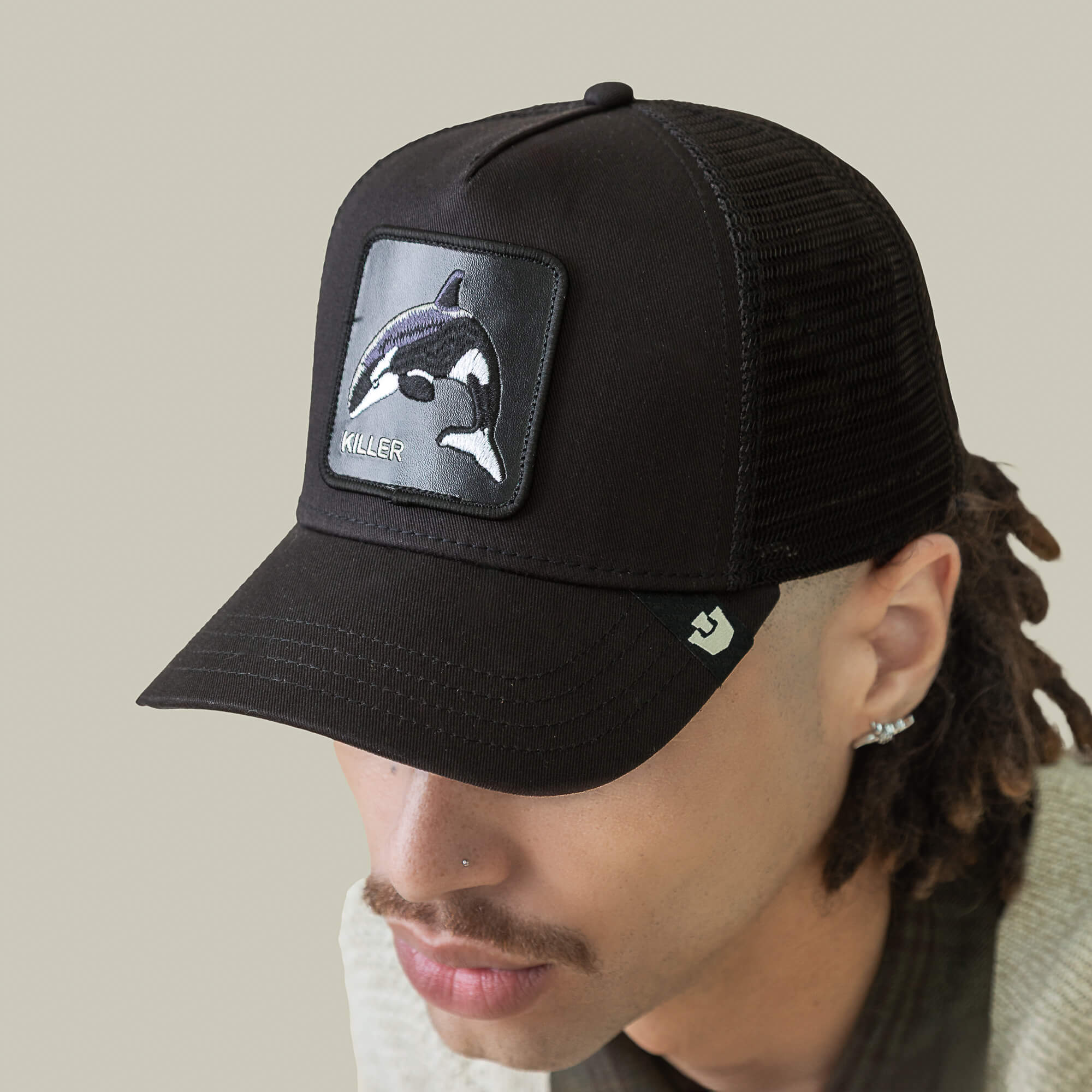 A person wearing the Goorin Bros. Killer Trucker cap—a black and white mesh-back hat with an apex stitched orca patch labeled KILLER on the front.