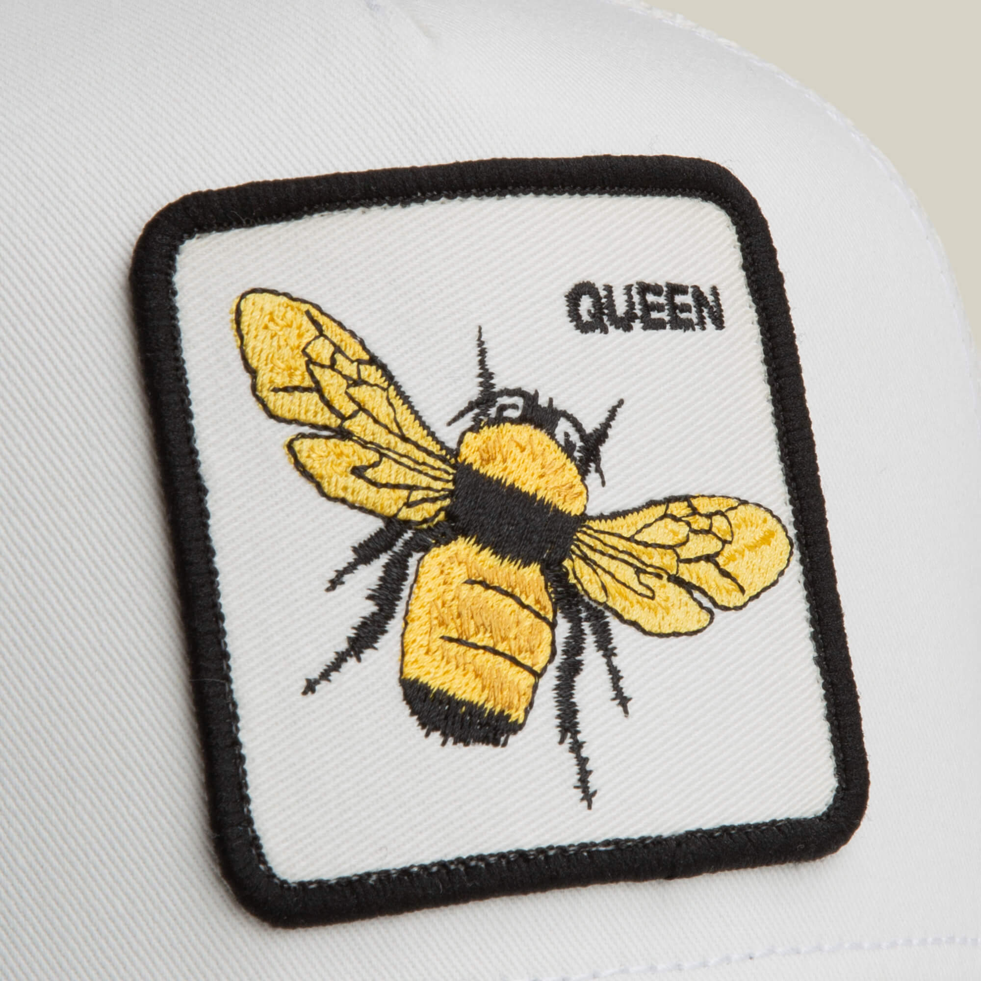 The Goorin Bros. Queen Trucker hat features a yellow and black embroidered bee with the word "QUEEN" on a white surface.