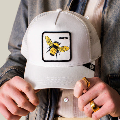 A person wearing the Goorin Bros. "Queen Trucker" cap, featuring a queen bee patch, holds the brim with both hands.