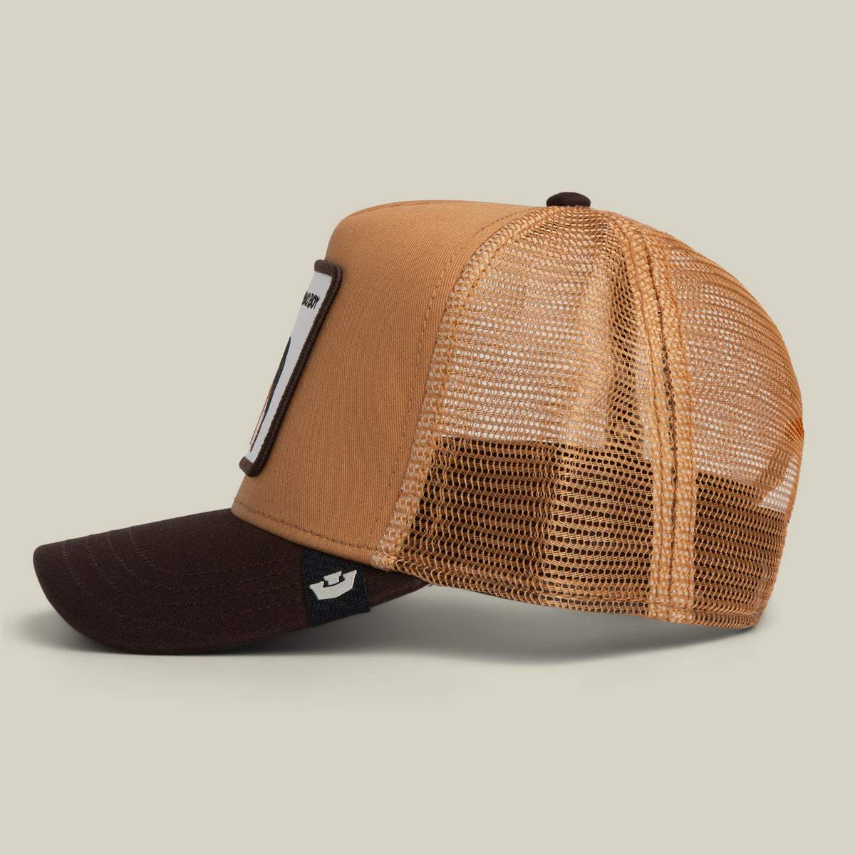 Side view of a brown and tan Bad Boy Trucker hat featuring a mesh back and a graphic patch on the front panel.
