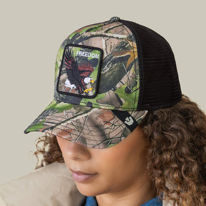 A person wearing Goorin Bros.’ Camouflage Eagle trucker hat, featuring eagle embroidery and a FREEDOM patch—ideal for fans of patriotic style.