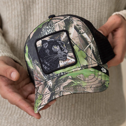 A person holds the Goorin Bros. Camouflage Panther trucker hat, featuring deep woods camo and a patch with a black panther above midnight-black "PANTHER" embroidery.