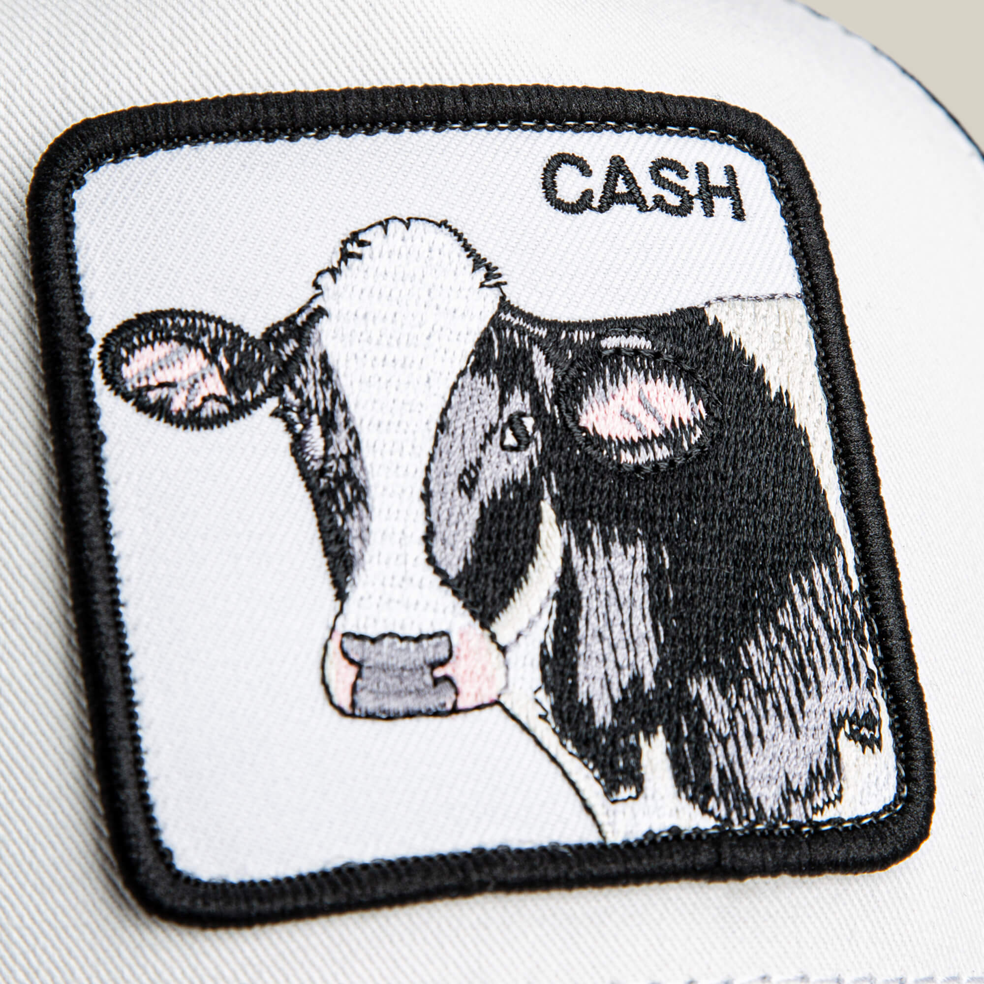 The Goorin Bros. Cash Cow Trucker features a bold patch with an embroidered black and white cow head and the word "CASH" in the top right—an ideal addition to any trucker hat collection.
