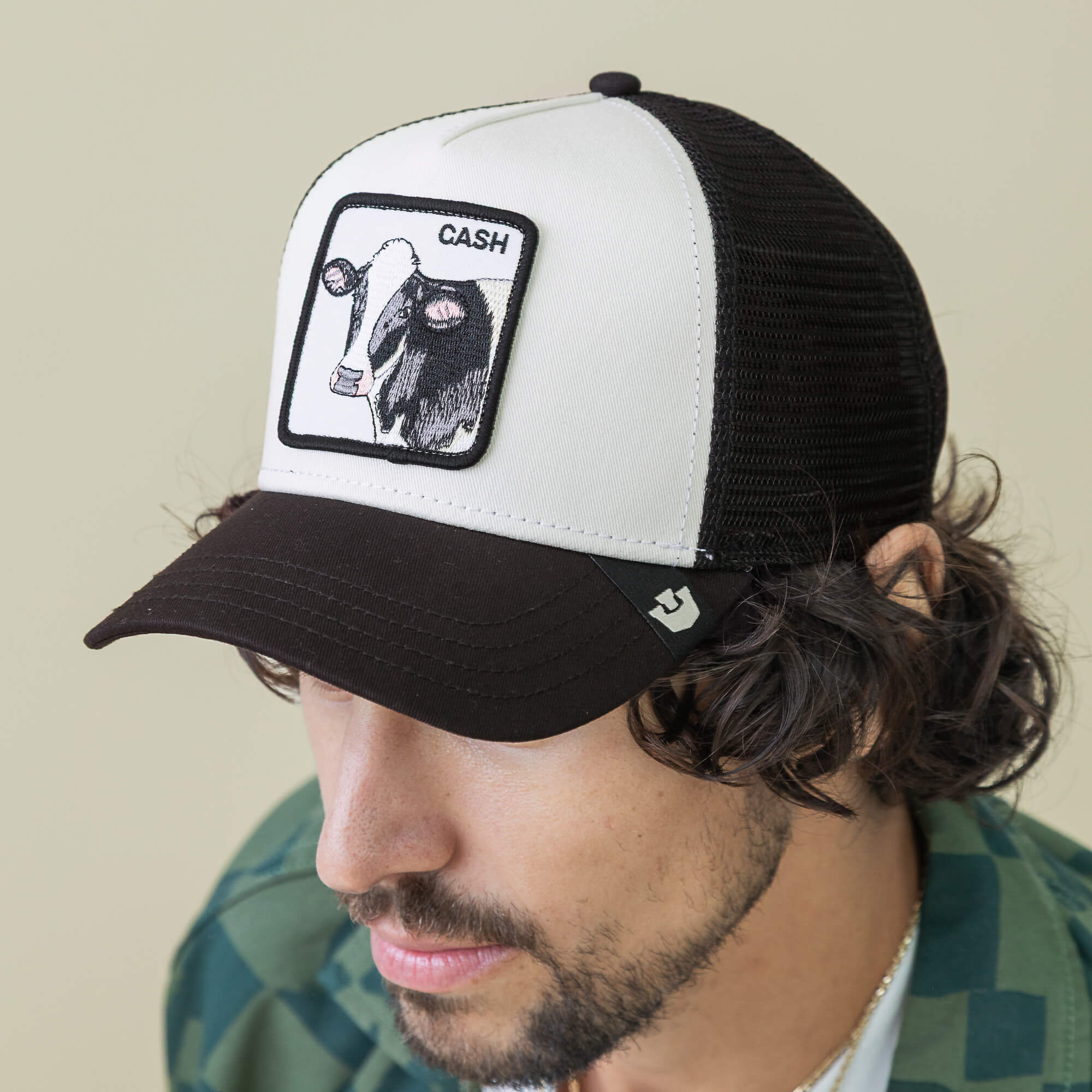 A man wears the Goorin Bros. Cash Cow Trucker hat, featuring a bold bovine patch, paired with a green plaid shirt.