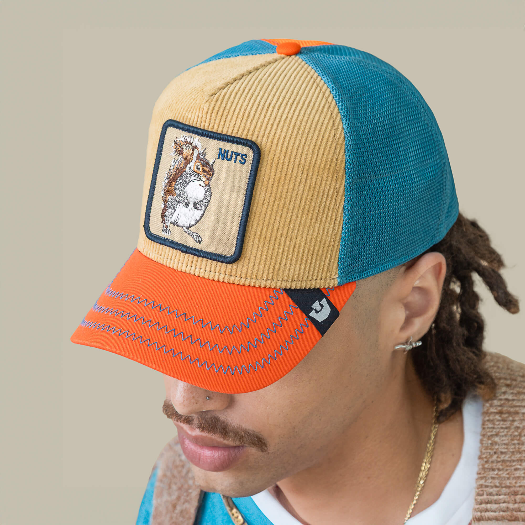 A person wearing the Goorin Bros. Nuts Remix hat, featuring a multicolored design, embroidered squirrel patch, "NUTS" on the front panel, and electric blue mesh that energizes their style.