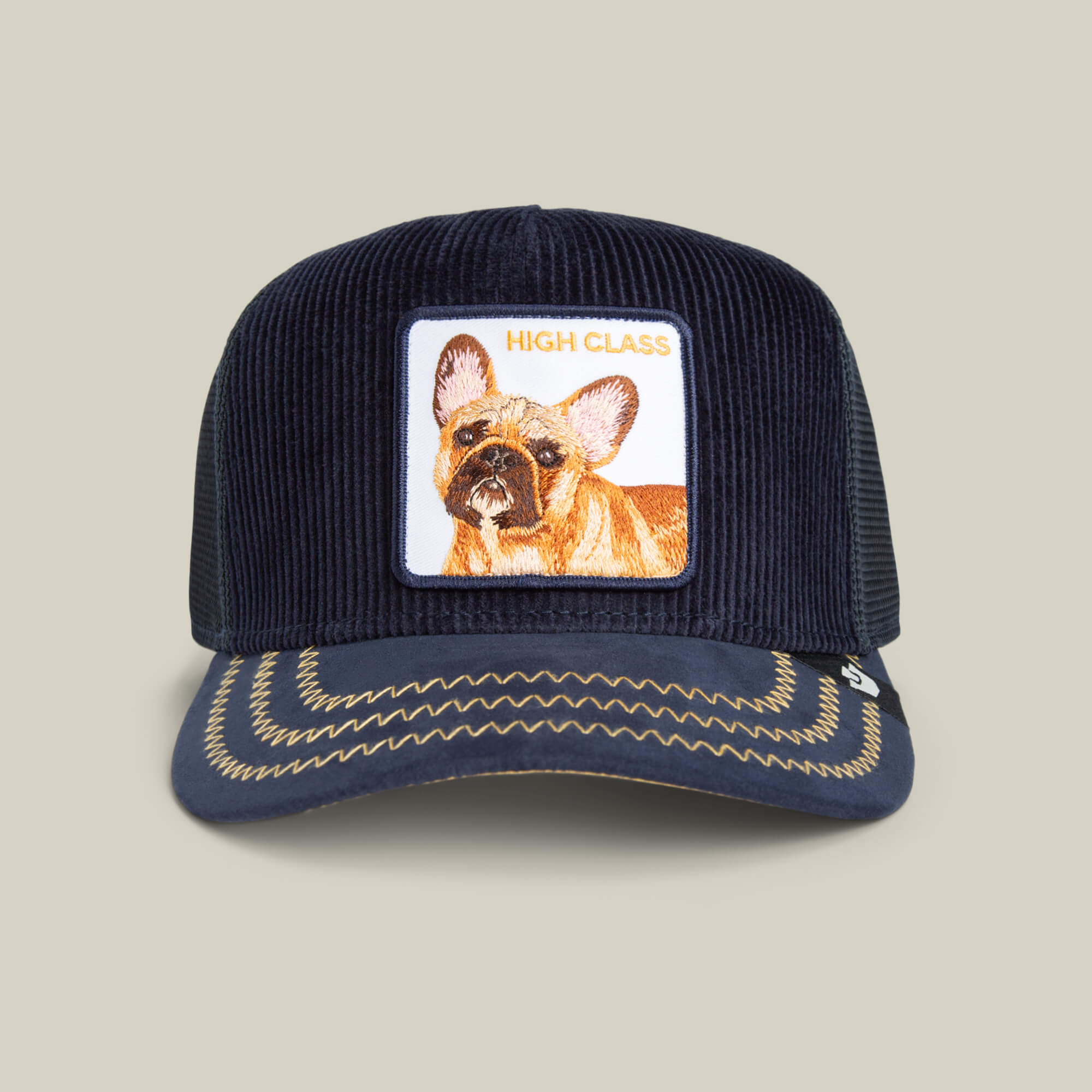 The Goorin Bros. High Class Remix cap is a navy blue corduroy hat with rich textures, a French bulldog patch labeled HIGH CLASS, and decorative brim stitching.