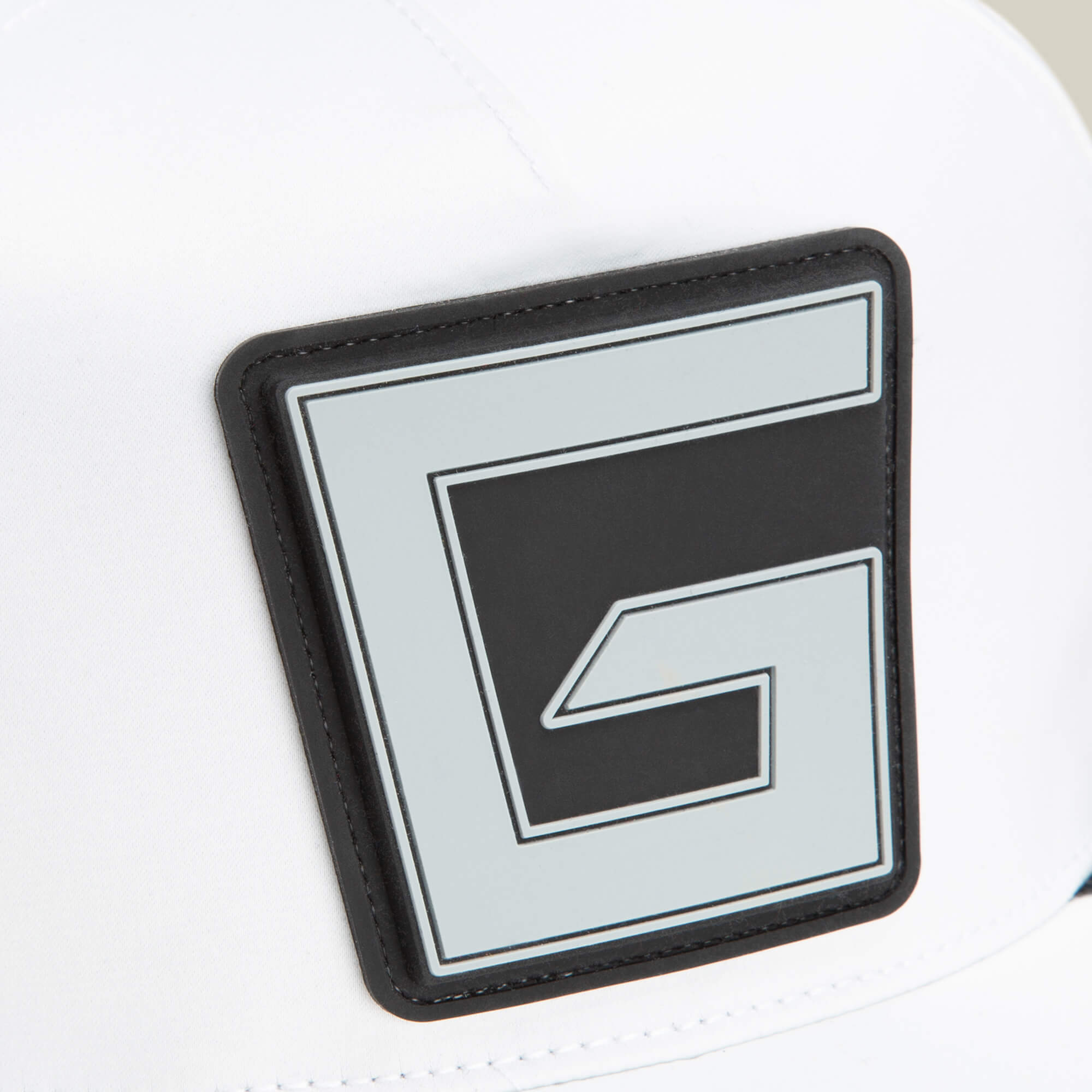 Close-up of a white Goorin Bros. Pole Position - Speedbump hat with a large, square black and gray patch featuring a stylized G design on the front.