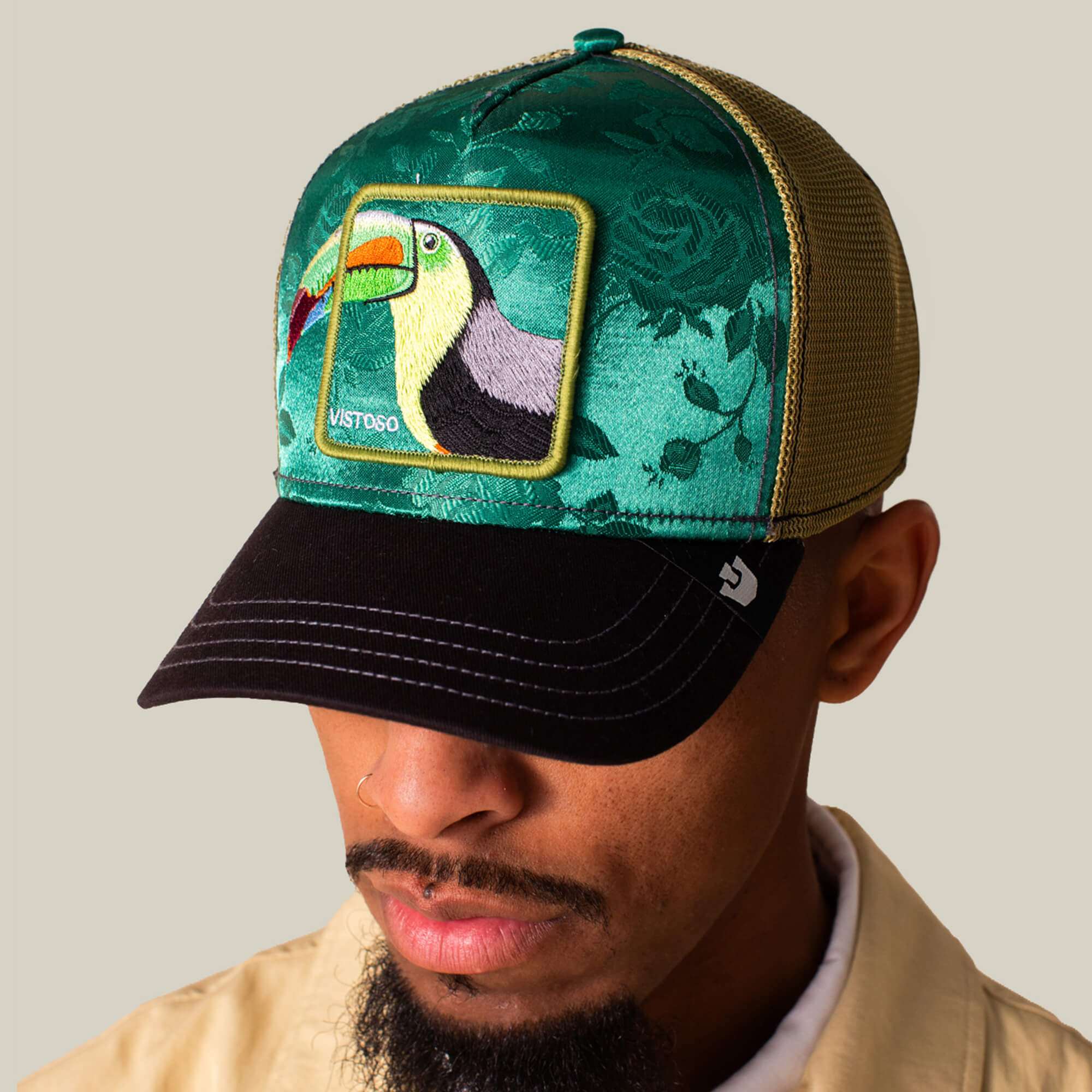 A man wears the Goorin Bros. Belize Toucan trucker cap, featuring a green crown, black brim, and an embroidered Belize Toucan patch on the front panel.