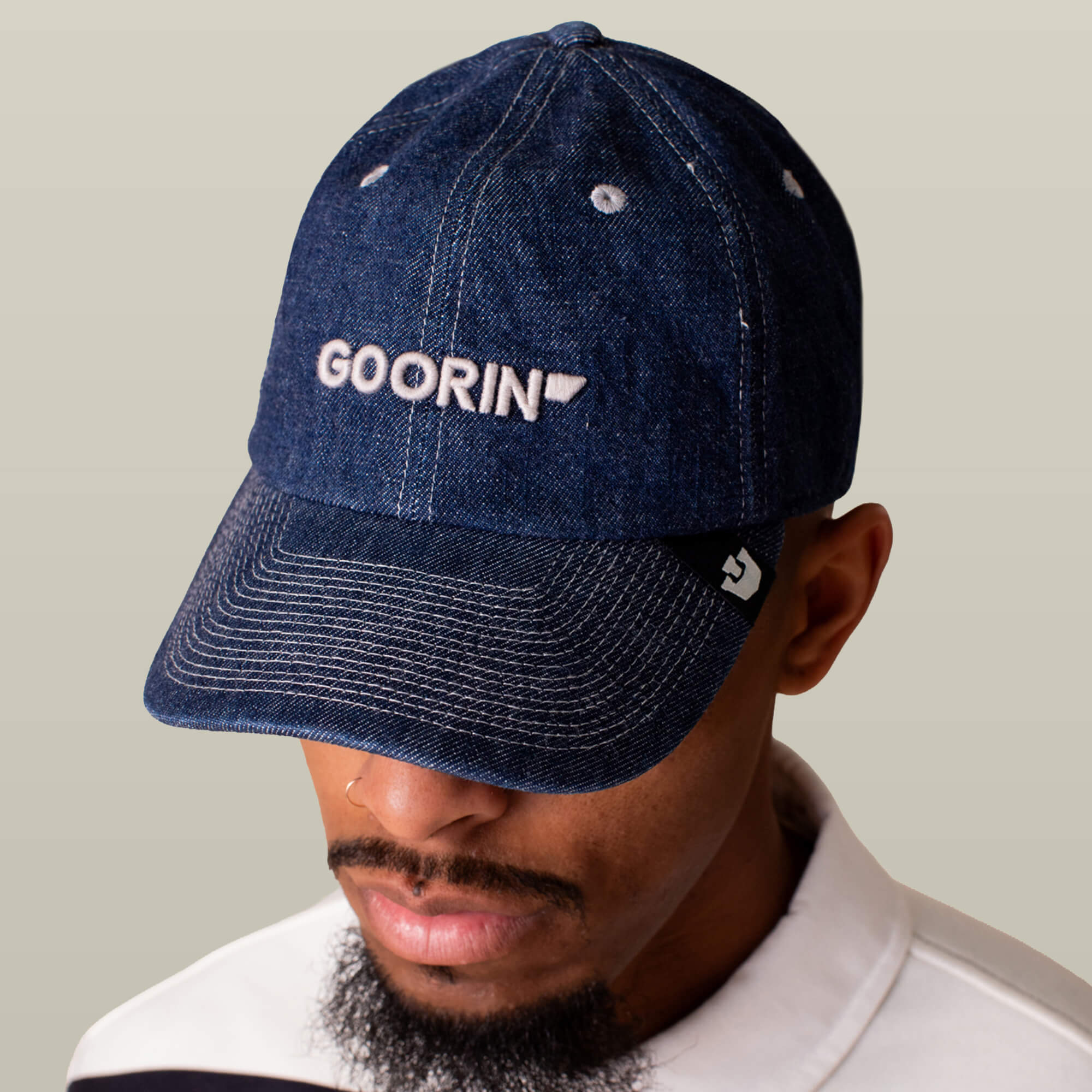 A man wears the Papa Core Denim hat by Goorin Bros., featuring a low-profile blue denim design and an embroidered wordmark on the front, as he looks downward against a plain light background.