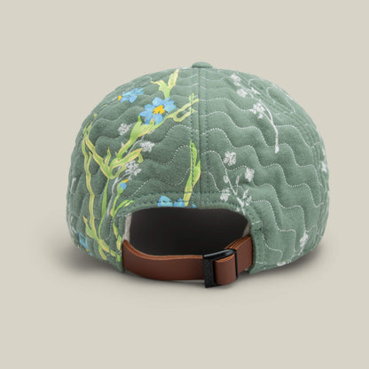 Back view of the Goorin Bros. Vol. 1 - Quiltbag: Laugh green OG Trucker cap, featuring quilted patchwork, floral design, brown adjustable strap, and black buckle against a neutral background.